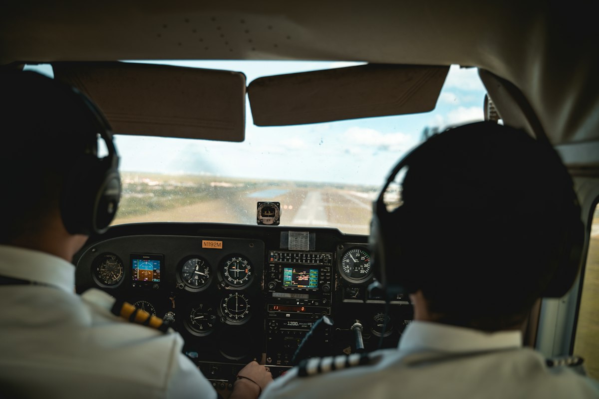 Deux pilotes vus de dos dans un cockpit, face au tableau de bord et à la piste